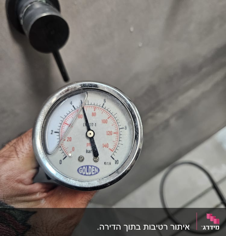 מד לחץ מים עם מחוגה על רקע קיר אפור